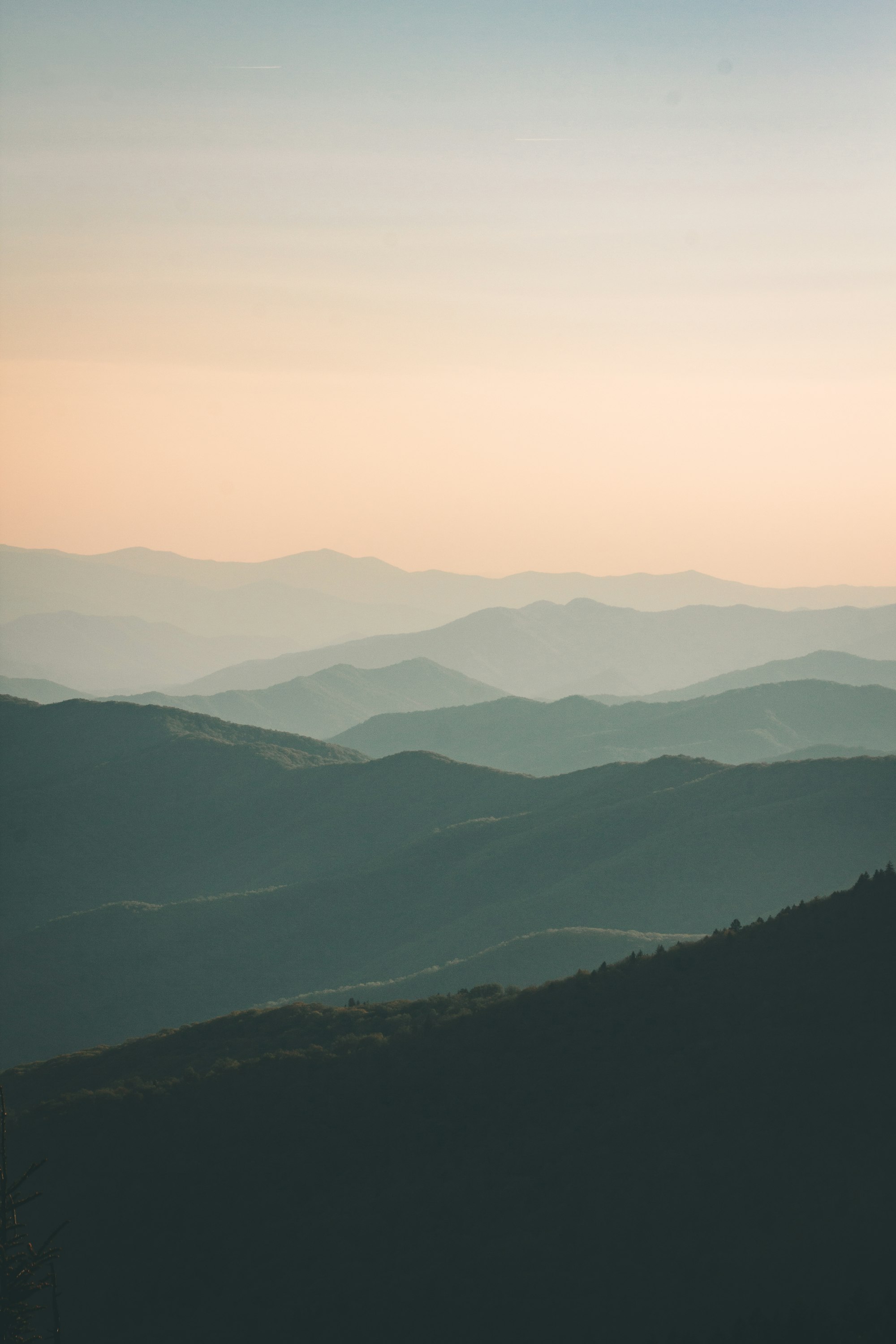Layered mountain ridges at dusk in muted sage and peach tones